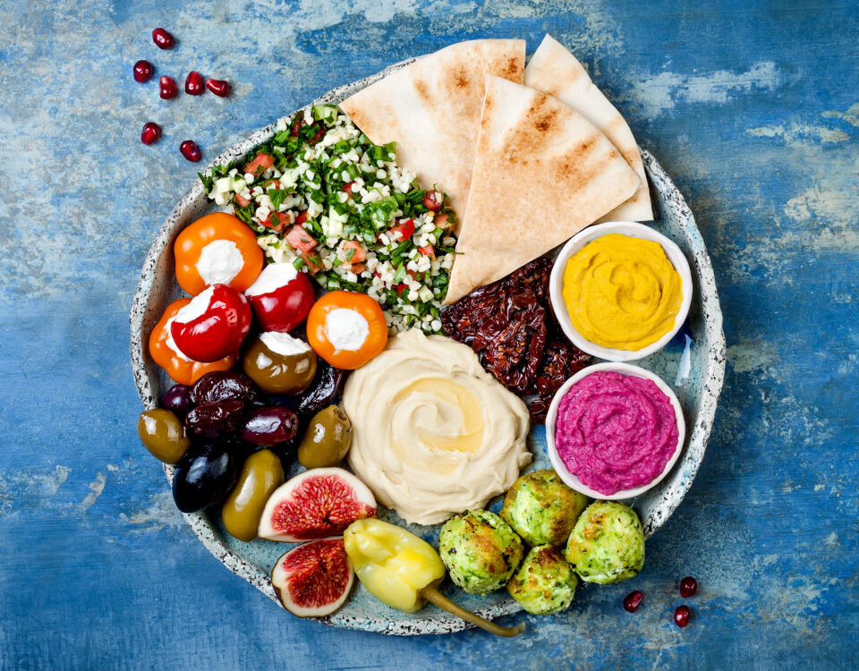 Middle Eastern meze platter with green falafel, pita, sun dried tomatoes, pumpkin and beet hummus, olives, stuffed peppers, tabbouleh, figs. Mediterranean appetizer party idea